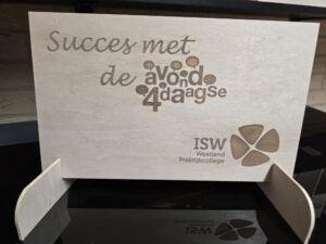 Houten plaquette op standaard met de Nederlandse tekst Succes met de avond4daagse en het logo van het ISW Westland Praktijkcollege erop gegraveerd.